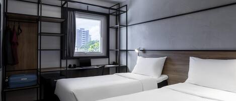 Quarto de hotel moderno com duas camas, uma escrivaninha, um guarda-roupa e uma janela grande com vista para a cidade.
