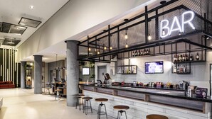 A modern bar area with a neon sign, bar stools, and a variety of beverages. - Ibis Botucatu (Botucatu)