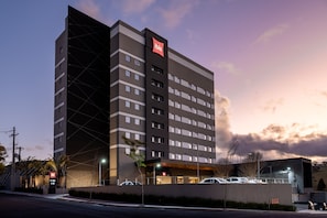 A modern hotel with a prominent 'ibis' sign, multiple floors, and a parking area with cars. - Ibis Botucatu (Botucatu)