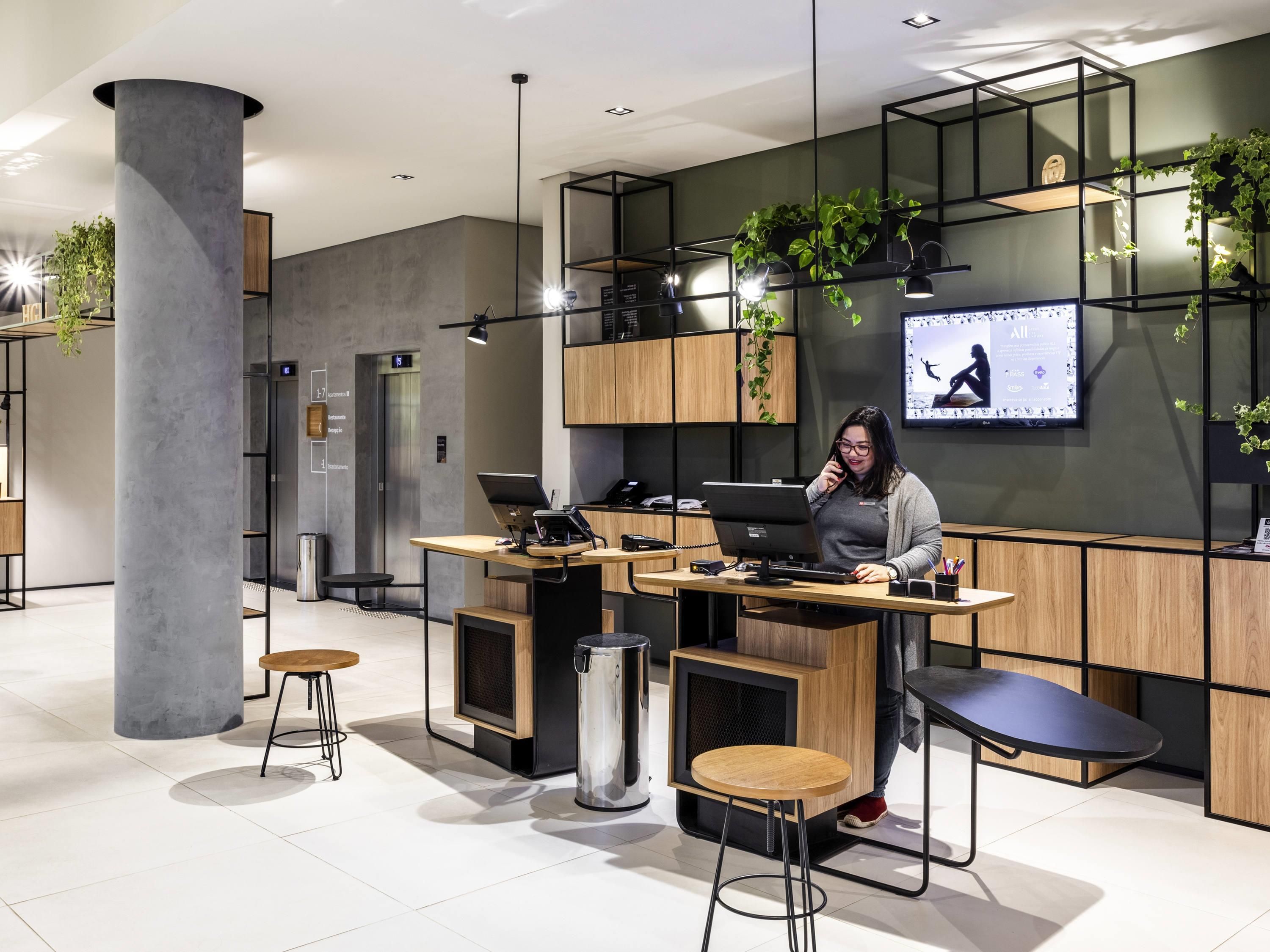 A modern office space with a reception desk, bar stools, a large screen, and plants.