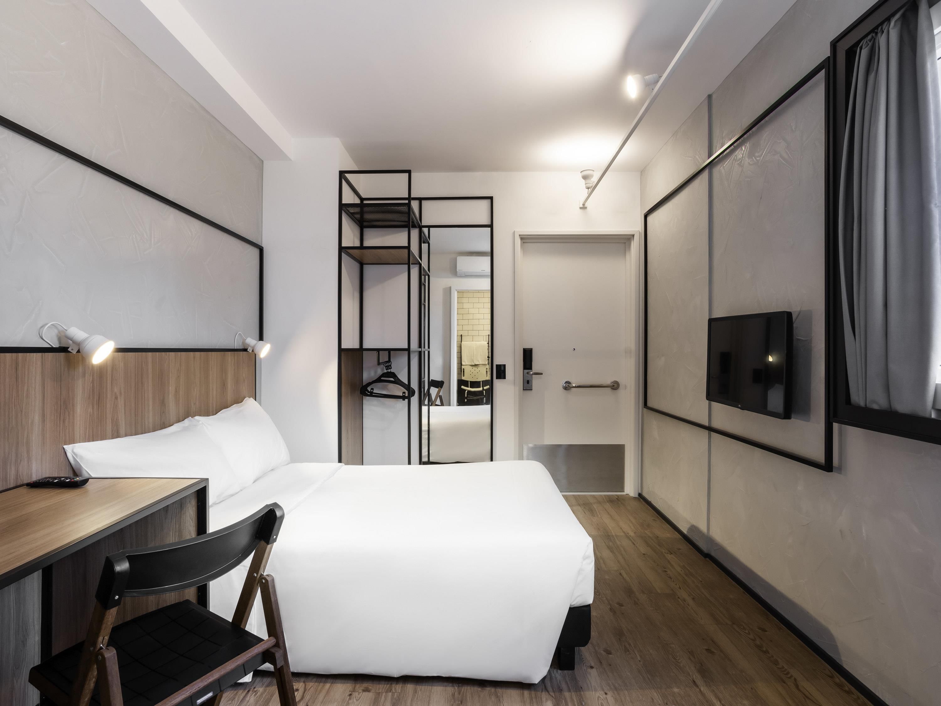 Een moderne hotelkamer met een bed, bureau, stoel, televisie en een inloopkast.