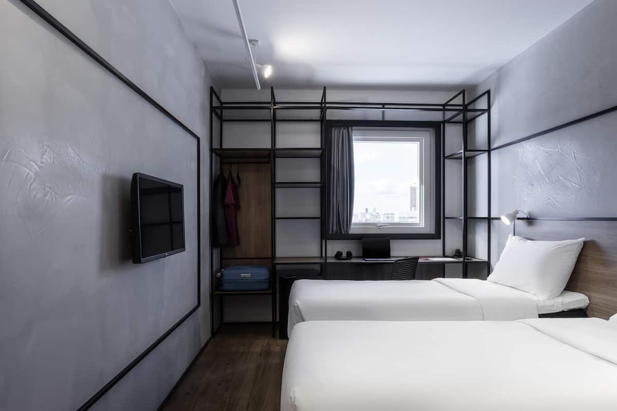 A modern hotel room with a bed, a desk, a TV, a wardrobe, and a city view.