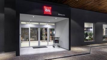 A modern hotel entrance with a prominent 'ibis' logo, a glass door entrance, and a visible elevator.