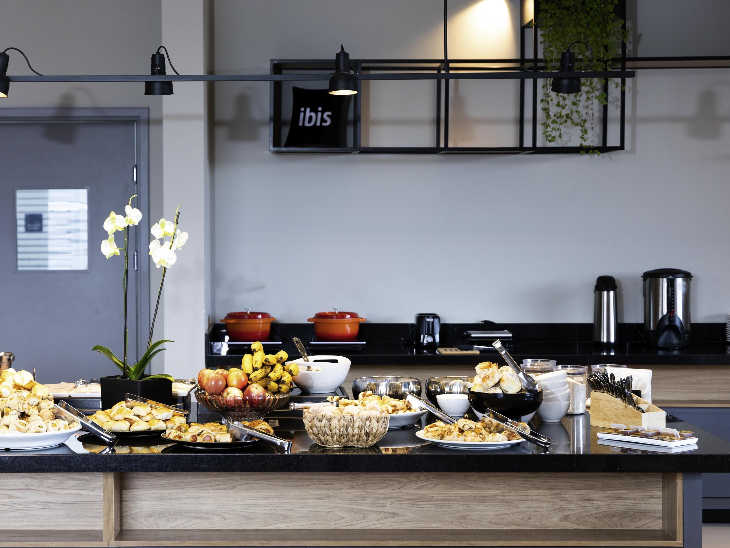 A modern kitchen with a black countertop, various food items, and a sign that reads "ibis".
