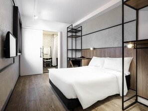 A modern hotel room with a bed, a desk, and a shower area.