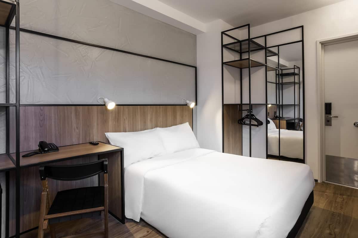 A hotel room with a bed, a desk, a chair, a phone, and a mirror.