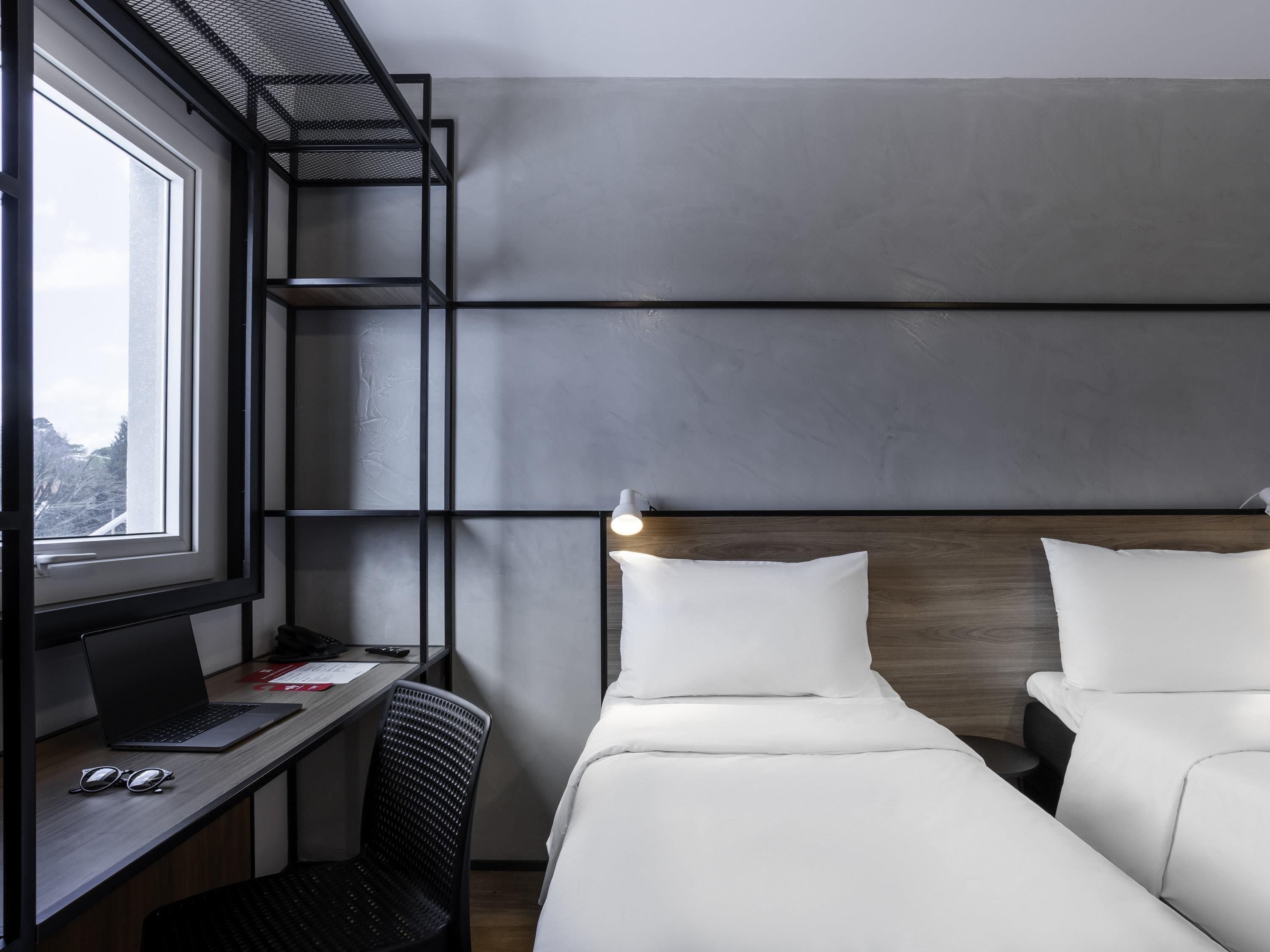Habitación de hotel con escritorio, dos camas, ventana y vistas al exterior.