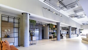A spacious lobby with a modern design, featuring a seating area with orange cushions, a reception desk, and a bar area. - Ibis Botucatu (Botucatu)
