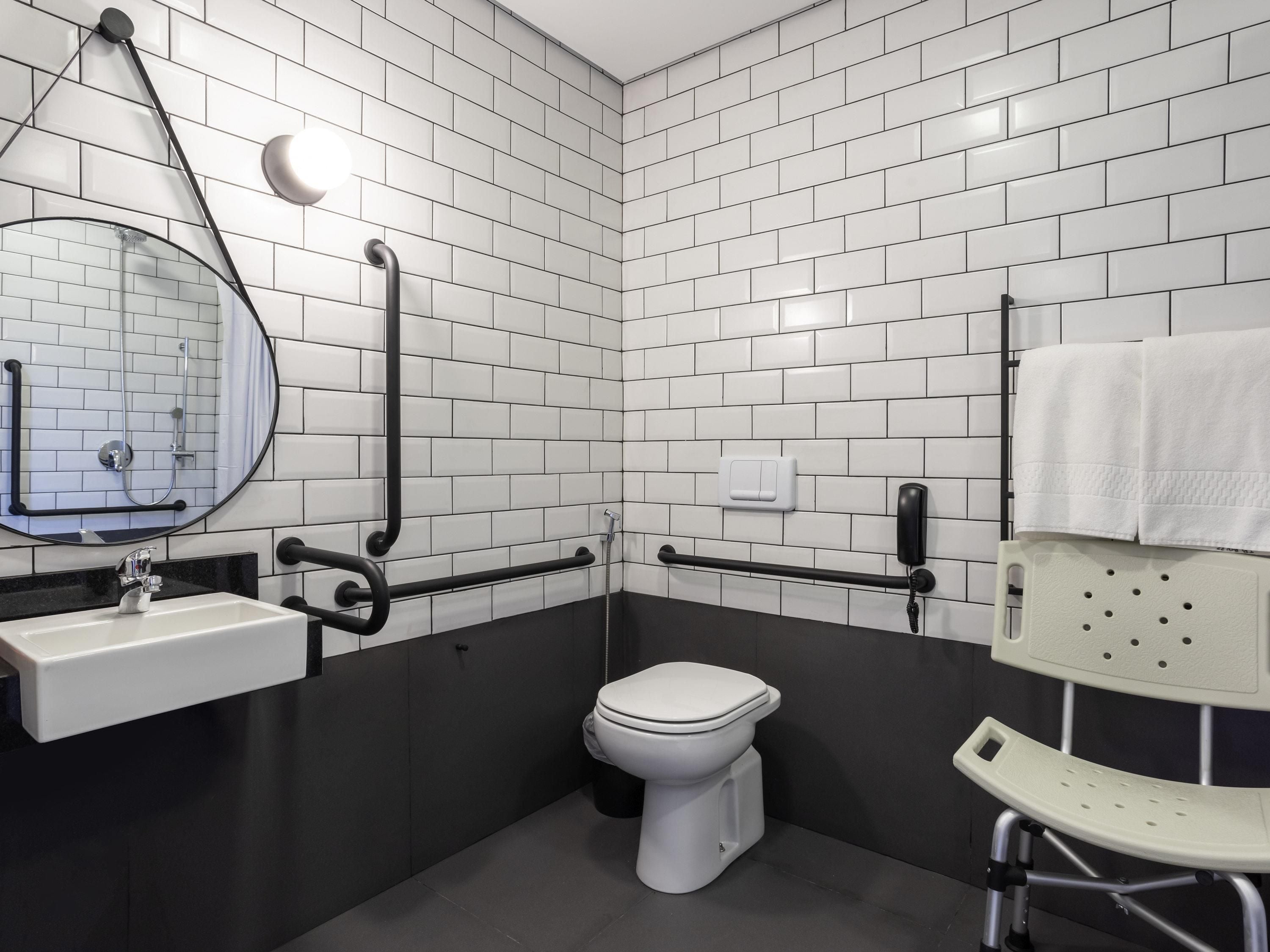 Casa de banho moderna com azulejos brancos tipo metrô, sanita branca, lavatório com espelho e um porta-toalhas.
