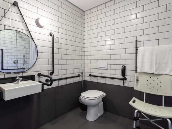 Une salle de bain moderne avec des carreaux de céramique blancs rectangulaires, des toilettes blanches, un lavabo avec un miroir et un porte-serviettes.