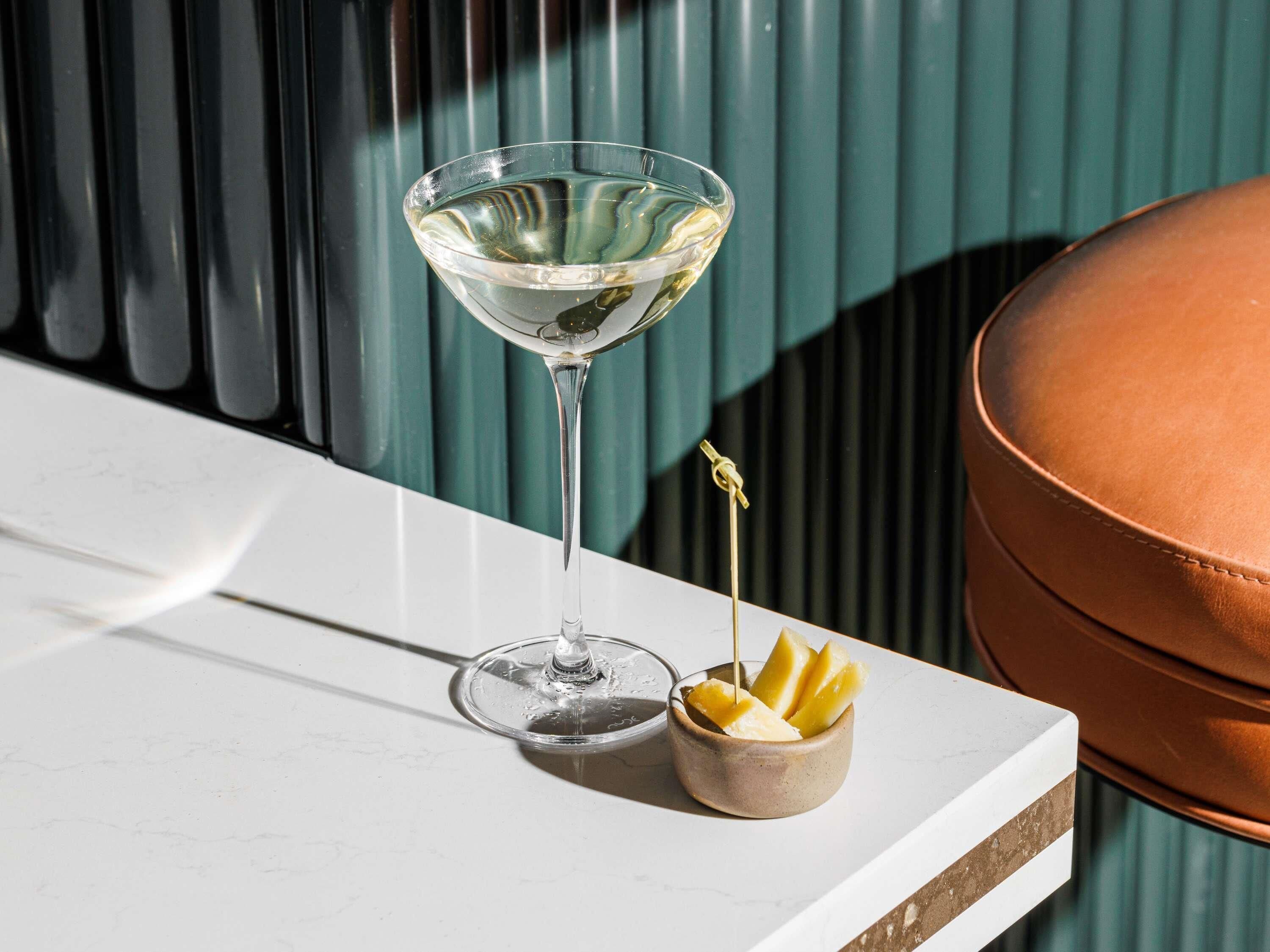 Una copa de martini con un adorno de limón sobre una superficie blanca, junto a un cuenco de terracota con rodajas de limón.