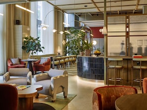 A modern lounge area with seating arrangements, a bar, and large windows allowing natural light. - Tribe London Canary Wharf (London)
