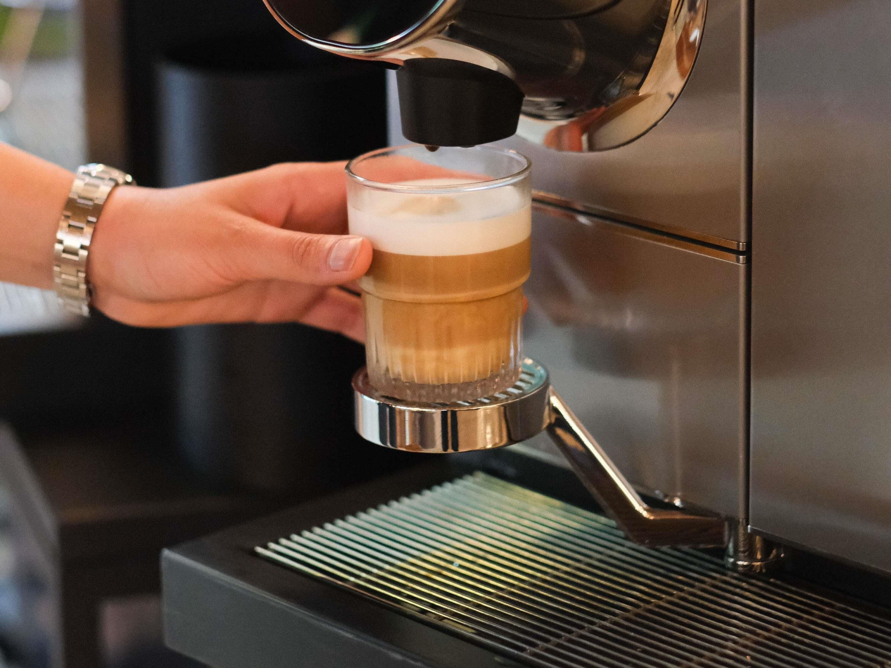 Une main tenant un verre dans lequel on verse une boisson provenant d’une machine à café.