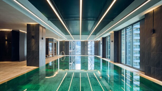 Een modern binnenzwembad met reflecterende oppervlakken, lineaire verlichting en grote ramen.