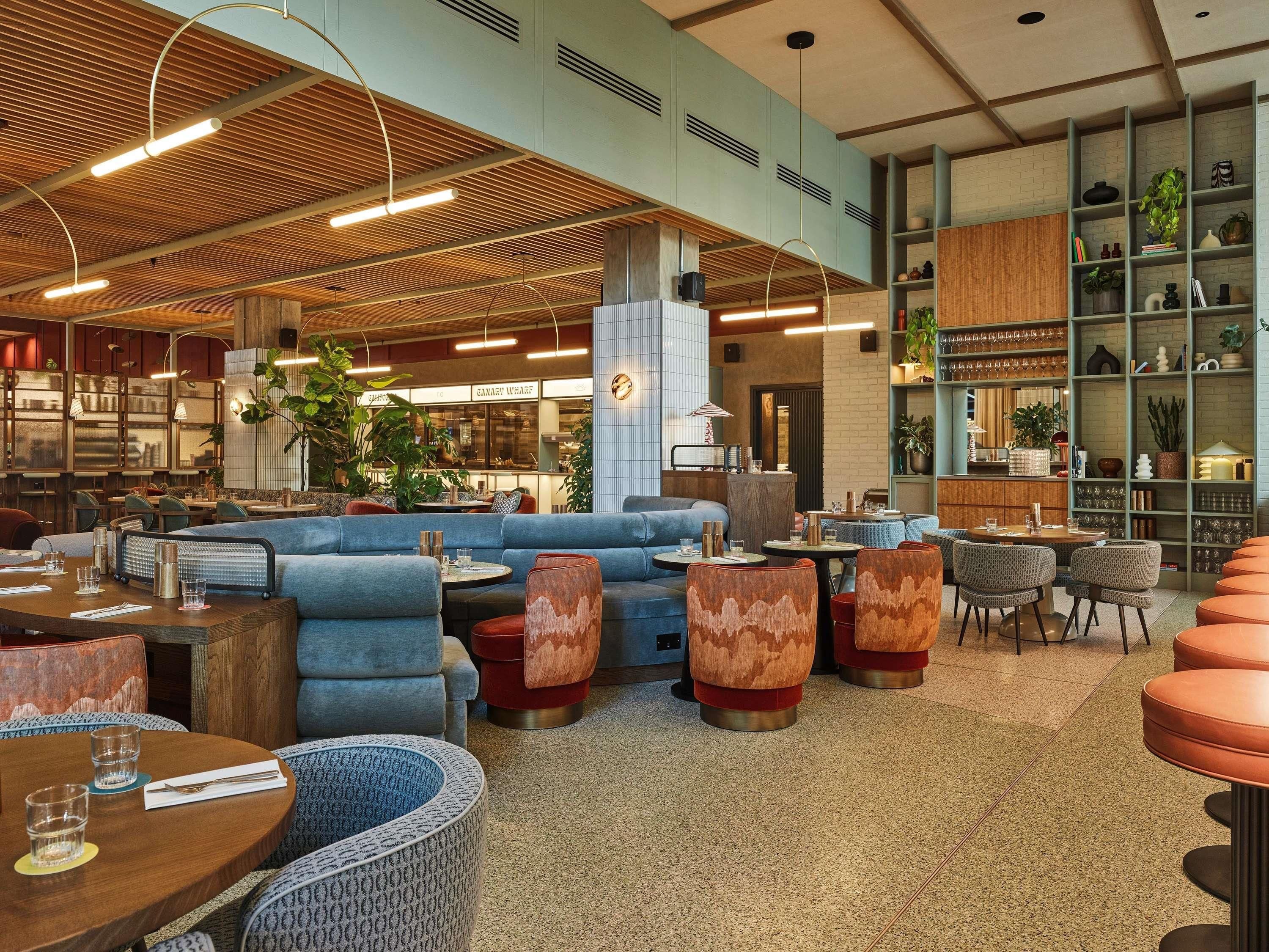 A modern interior with seating arrangements, a bar area, and a visible restaurant in the background.