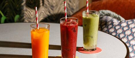 Three beverages on a round table with a patterned cushion in the background.