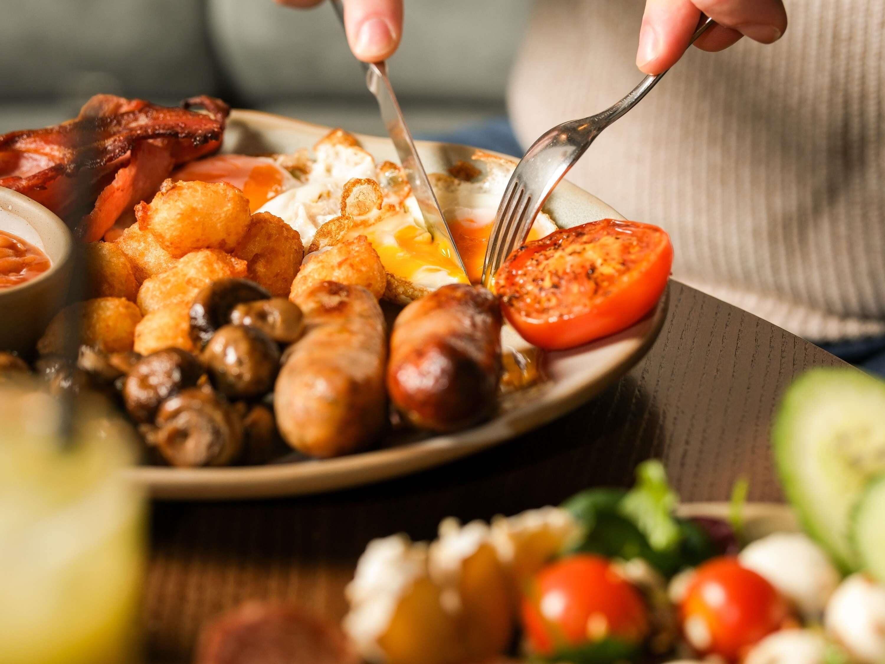 Une assiette de nourriture contenant divers éléments, notamment des saucisses, des champignons et une tranche de tomate.