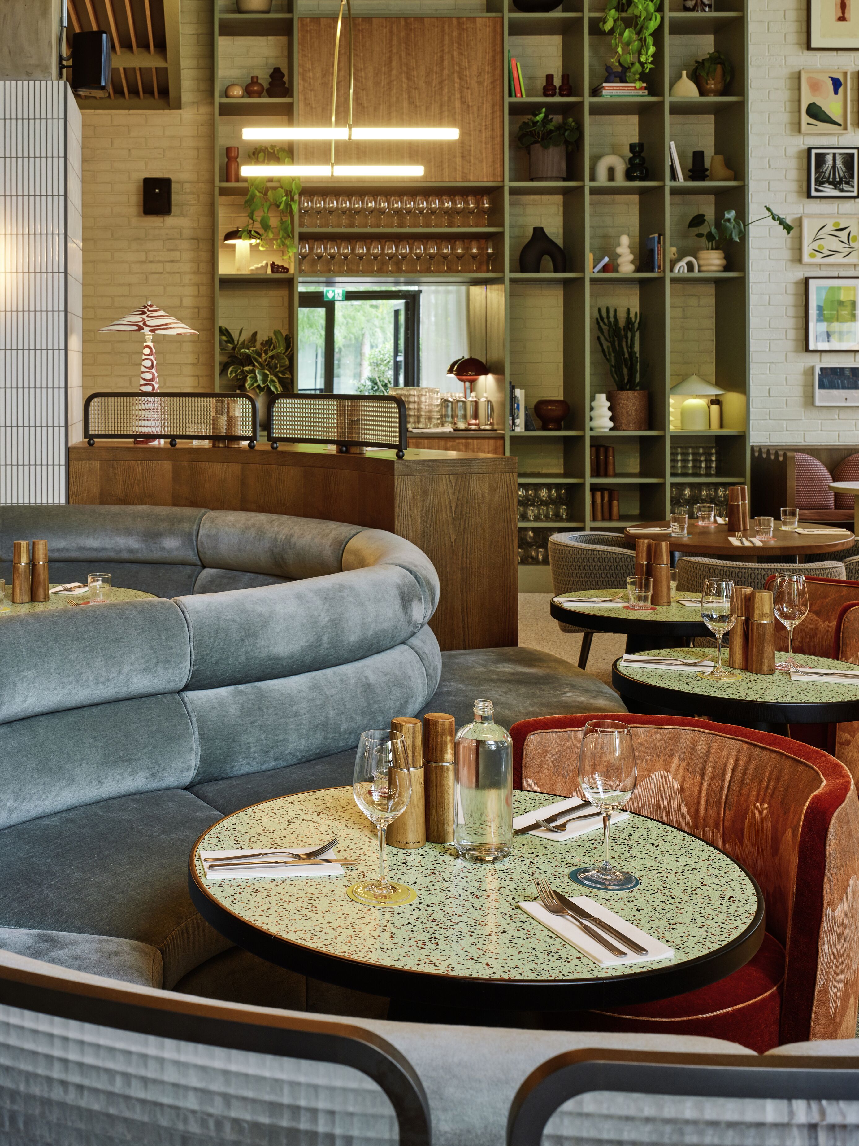 Un restaurante con mesas redondas, asientos acolchados y varios objetos decorativos en estanterías.