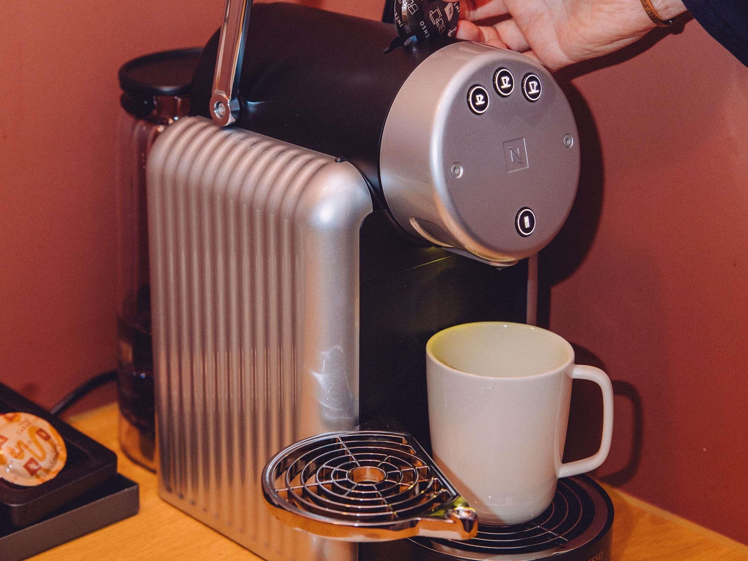 Une machine à café avec une tasse de café posée sur un sous-verre, une bouilloire et un petit récipient sur une table.