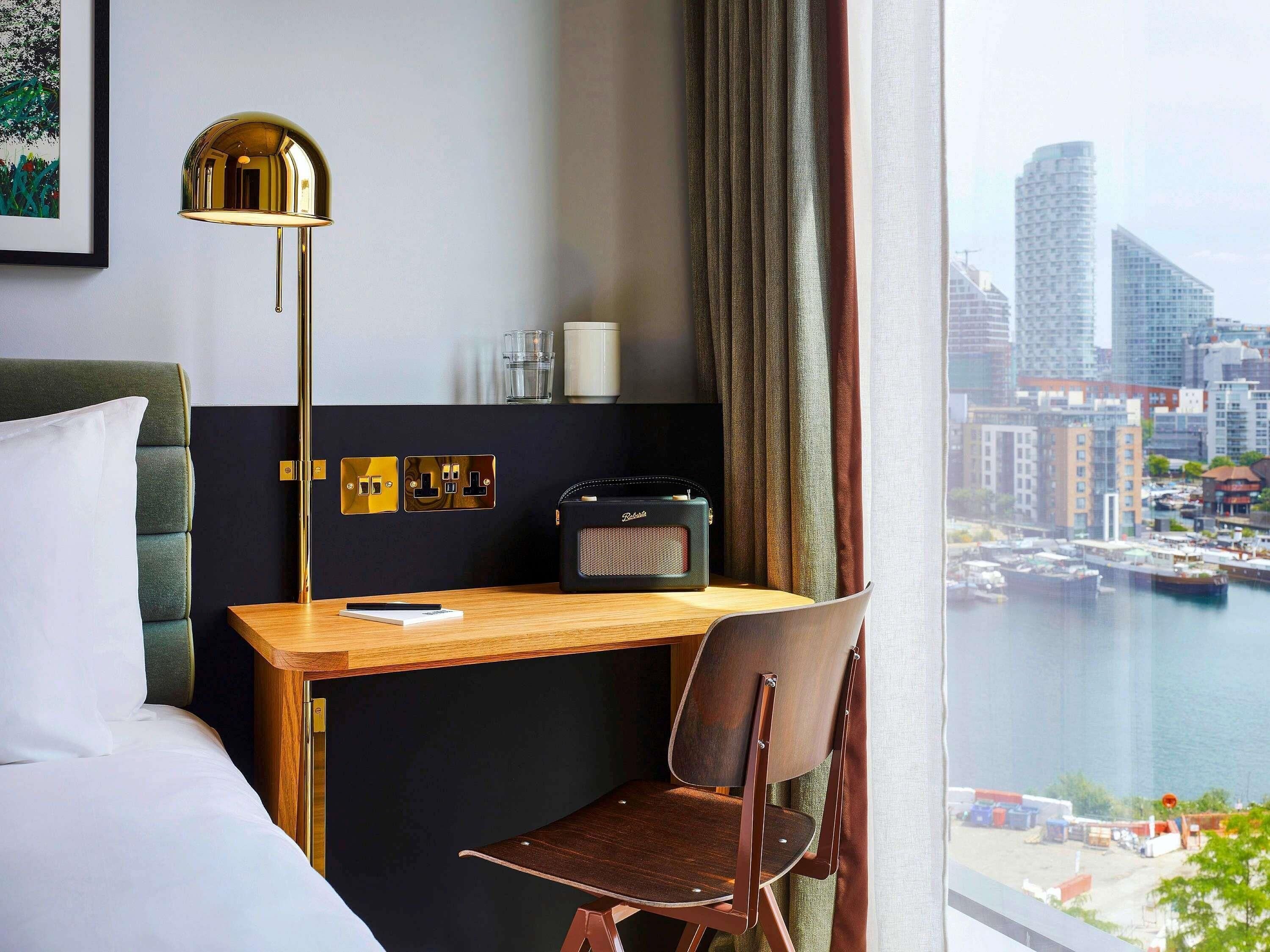 Habitación de hotel con cama, escritorio, silla, lámpara, radio y vista a la ciudad y al agua.