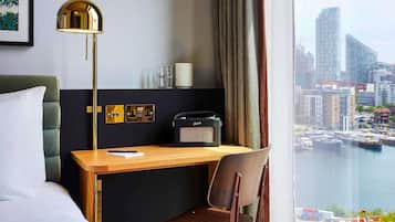 Habitación de hotel con cama, escritorio, silla, lámpara, radio y vista a la ciudad y al agua.