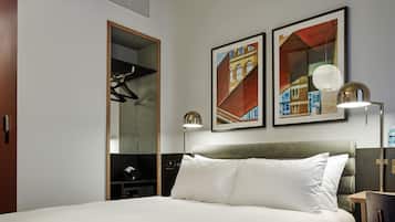 Une chambre d’hôtel comprenant un lit, deux lampes fixées au mur, un miroir et deux œuvres d’art encadrées.