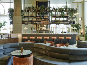 A bar area with multiple seating options, including a curved sofa and stools, and a bar counter with a variety of bottles and plants.