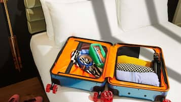 A bed with white pillows and a blue suitcase with red wheels on it.