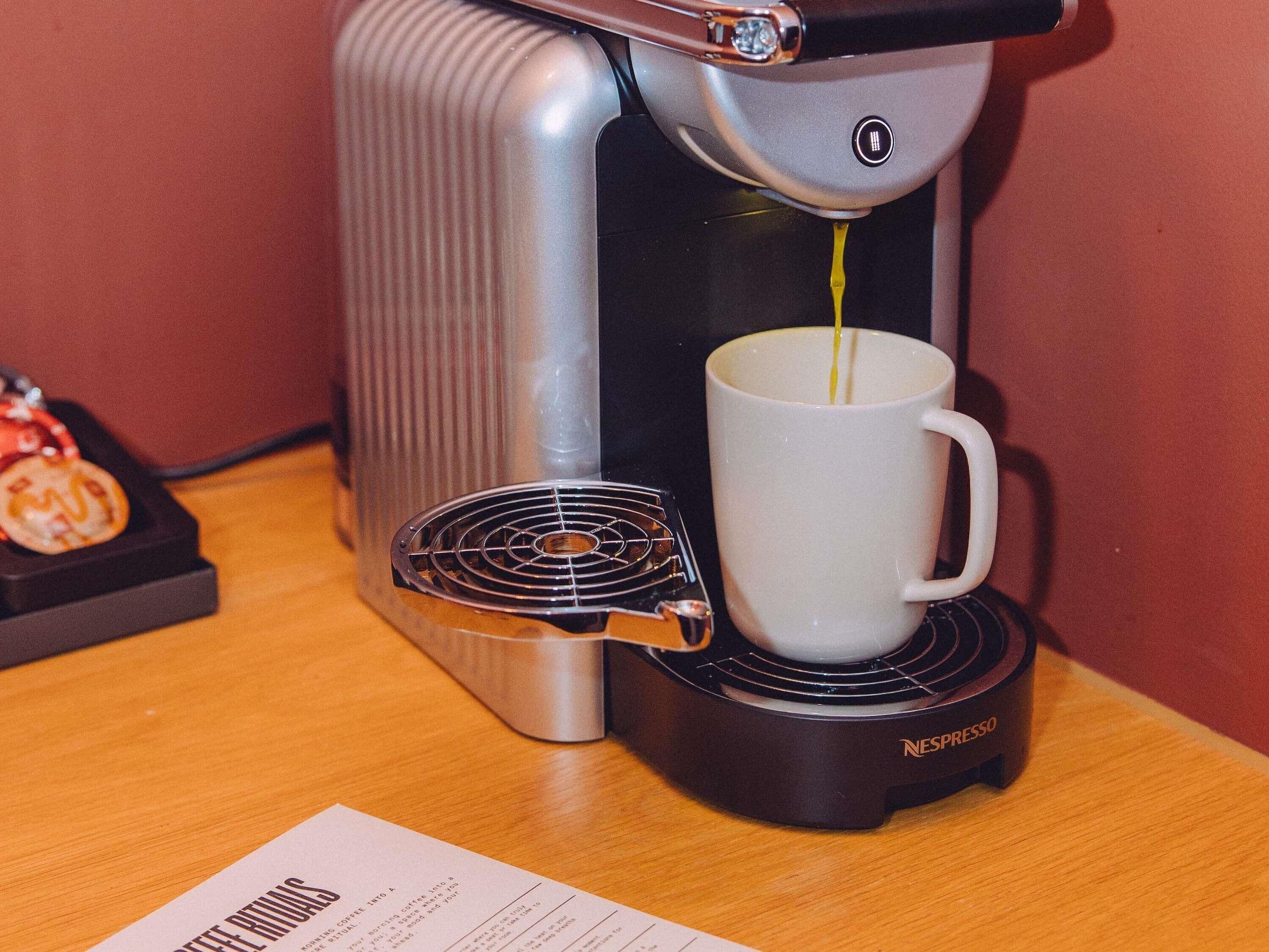 A Nespresso coffee machine on a table with a white cup and a menu.