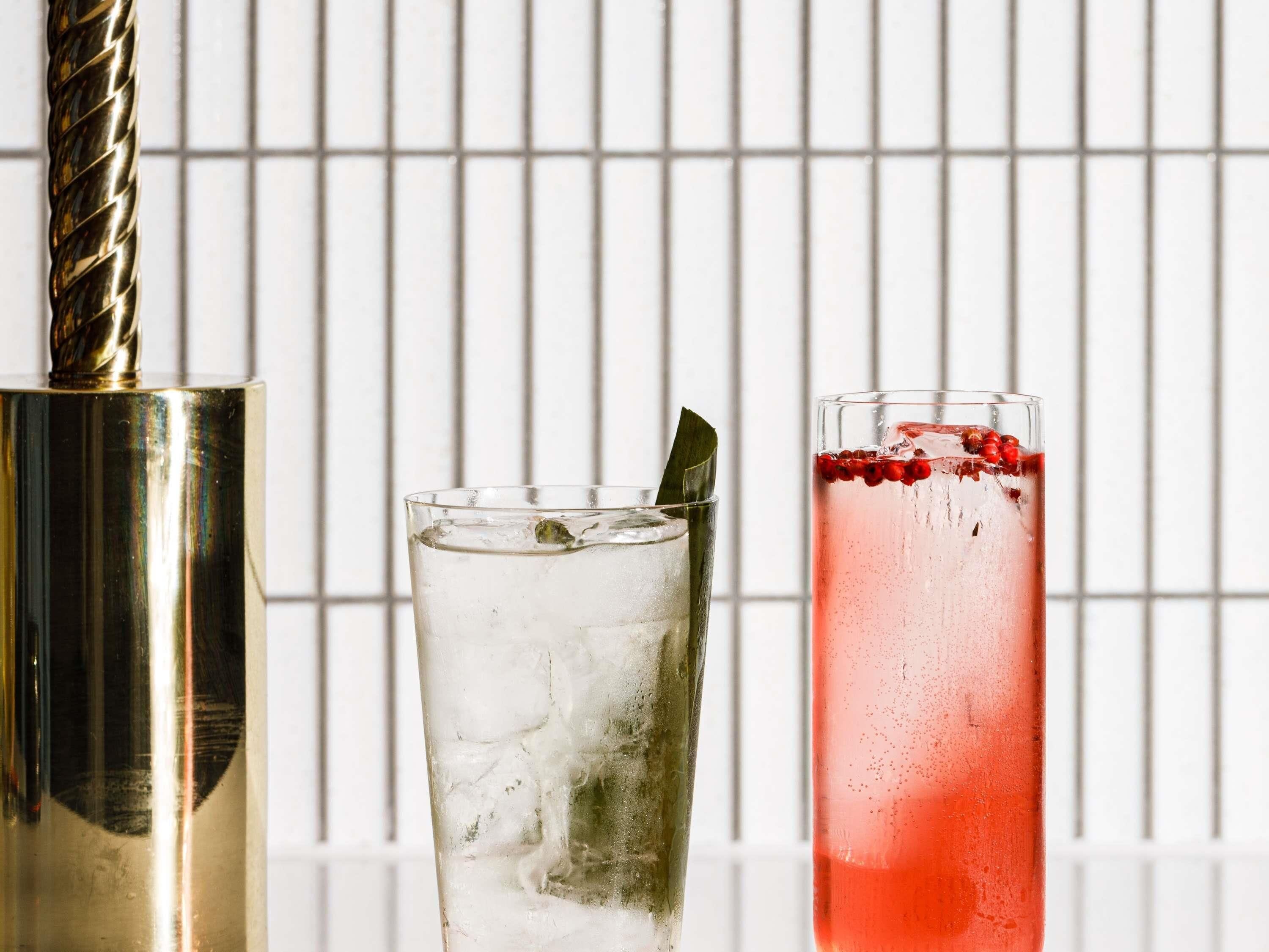 A cocktail shaker, a glass with ice and a straw, and a tall glass with a red drink and berries.