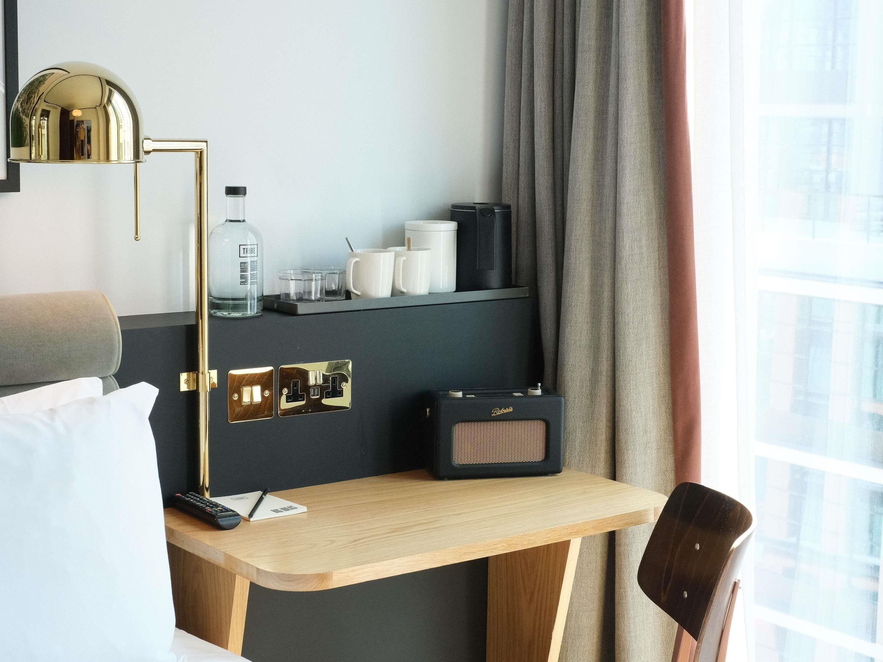 A hotel room with a desk, a chair, a bed, a lamp, a minibar, and a window with curtains.
