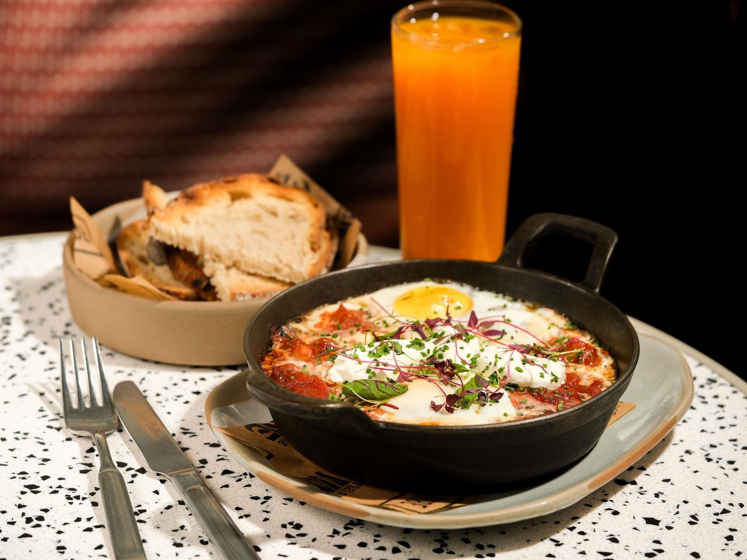 A meal with a bowl of food, a glass of orange juice, and a plate with cutlery on a speckled table.