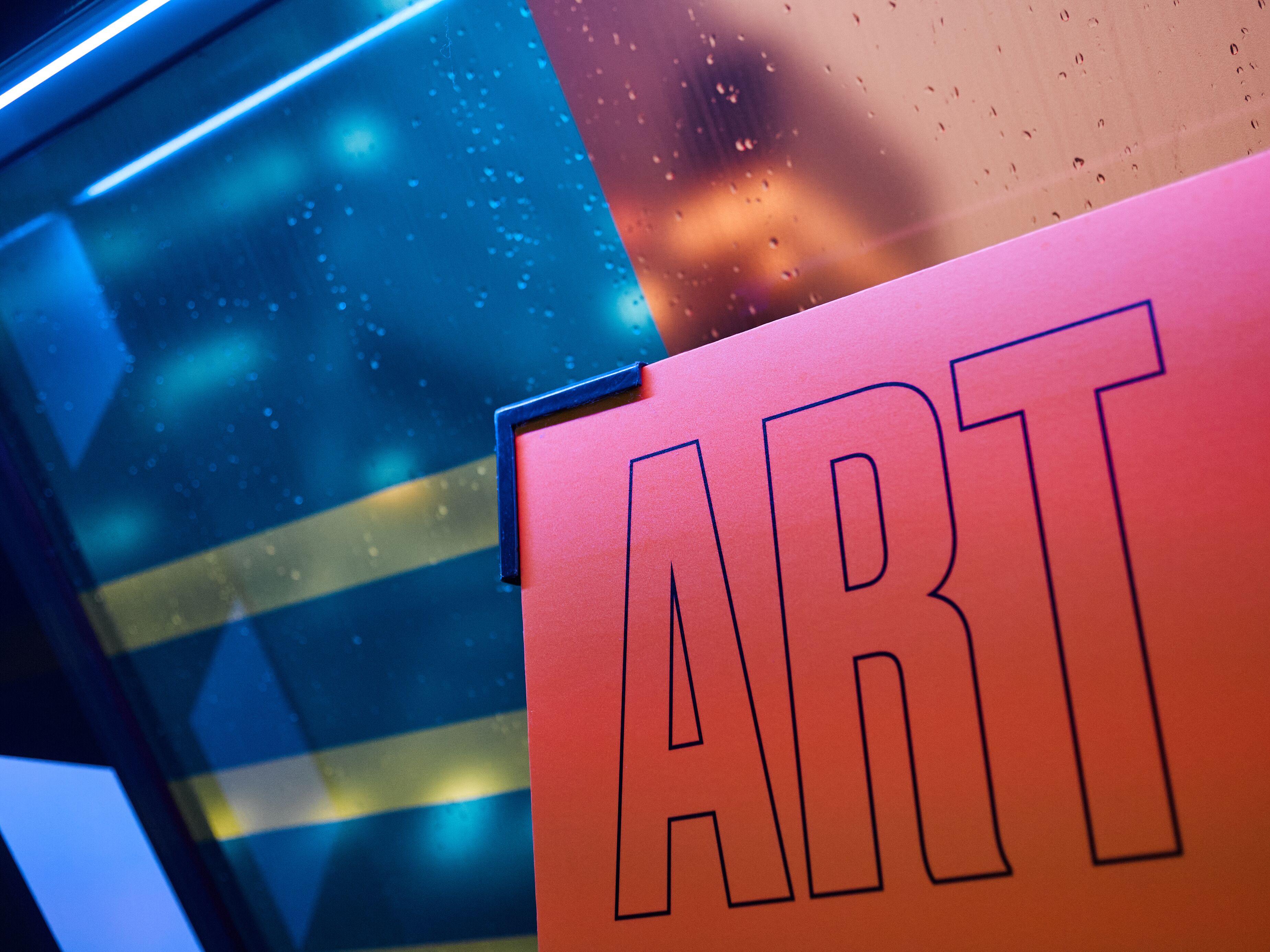 Ein Detailaufnahme eines Schildes mit dem Wort 'ART' in Fettschrift, das an einer Wand mit reflektierender Oberfläche angebracht ist.