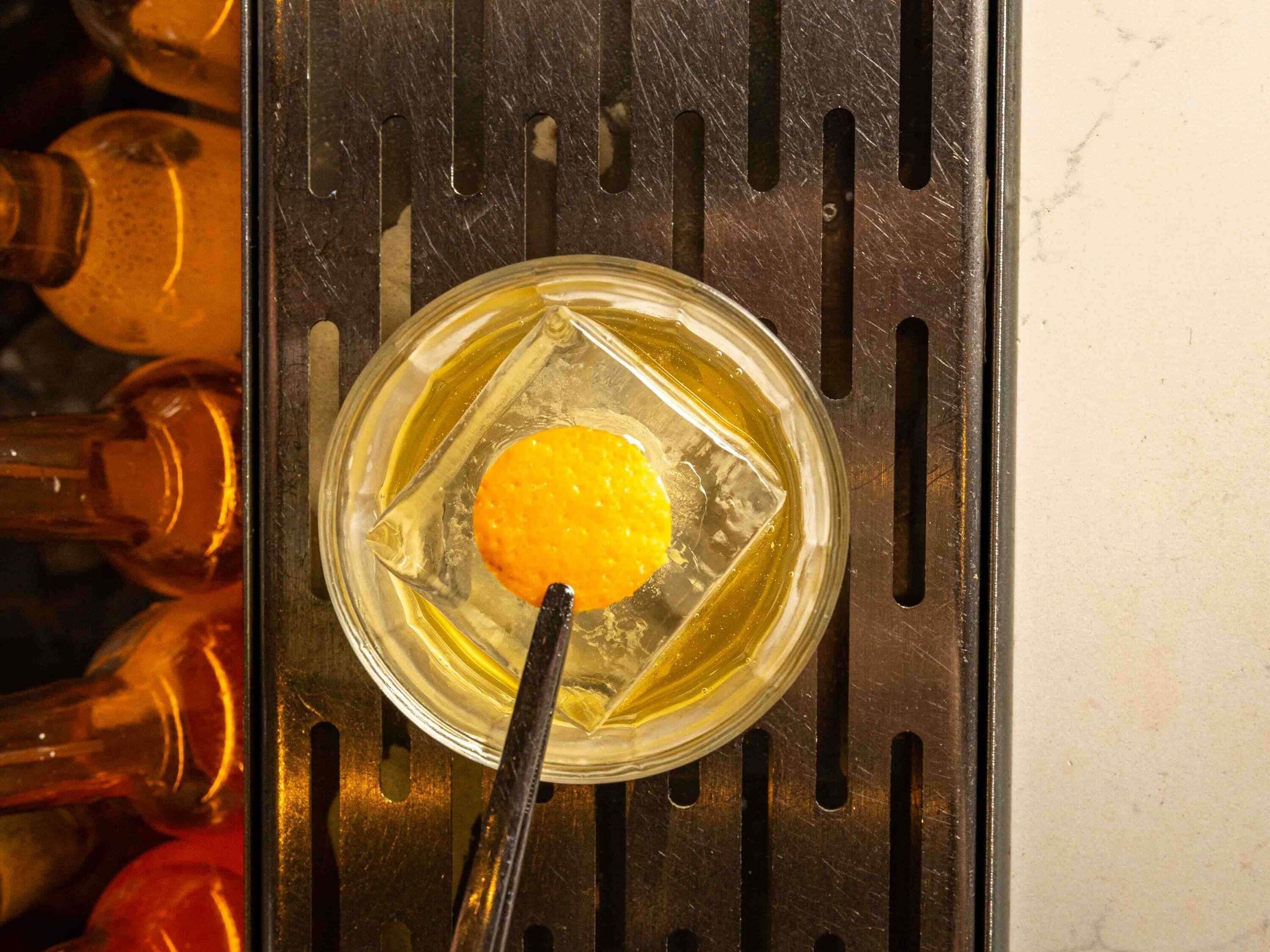 Un verre contenant un liquide jaune et un jaune d’œuf, posé sur une surface métallique dotée de fentes.