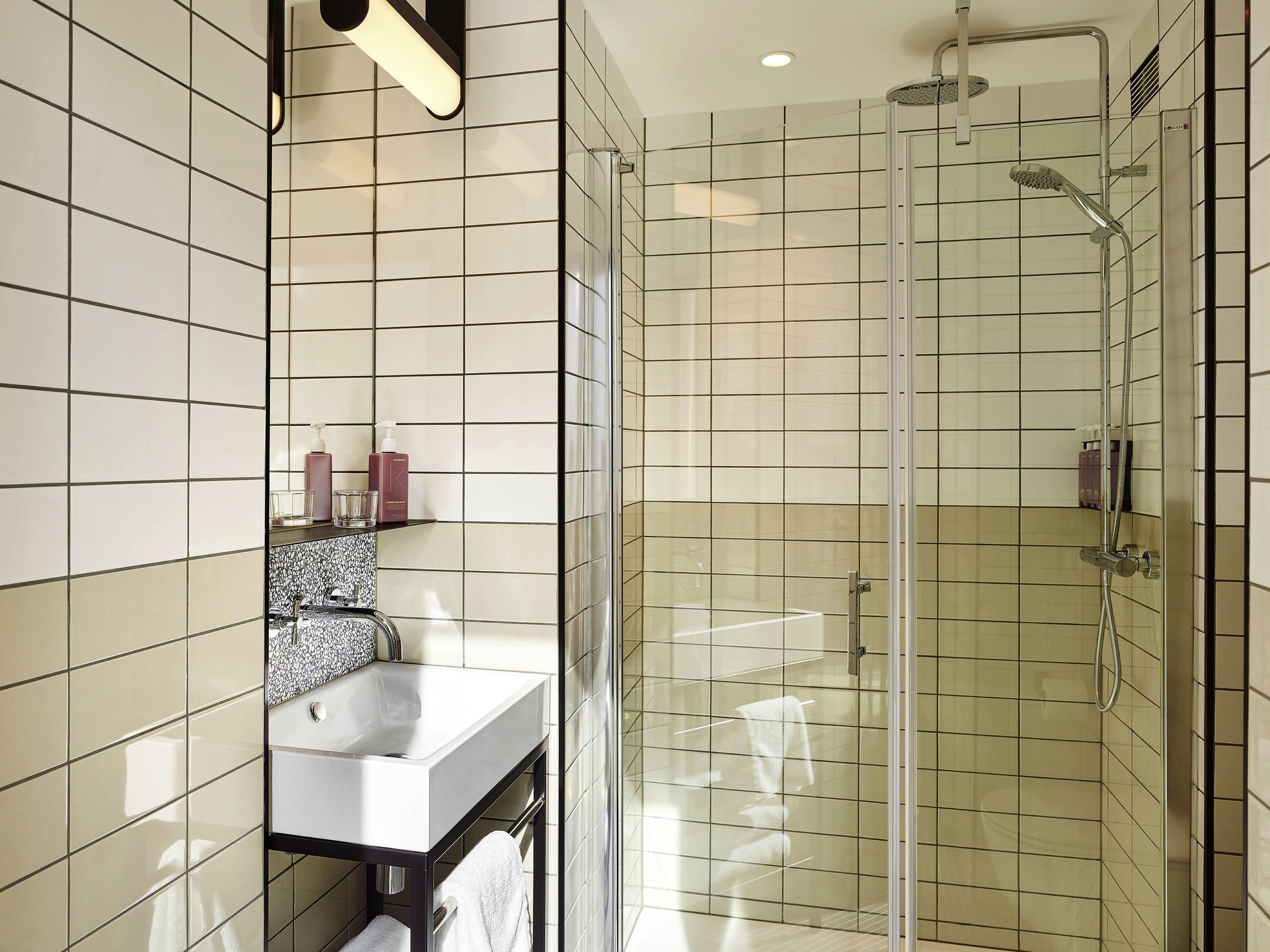 Un baño moderno con ducha de vidrio, un lavamanos blanco y un espejo con zócalo blanco y negro.
