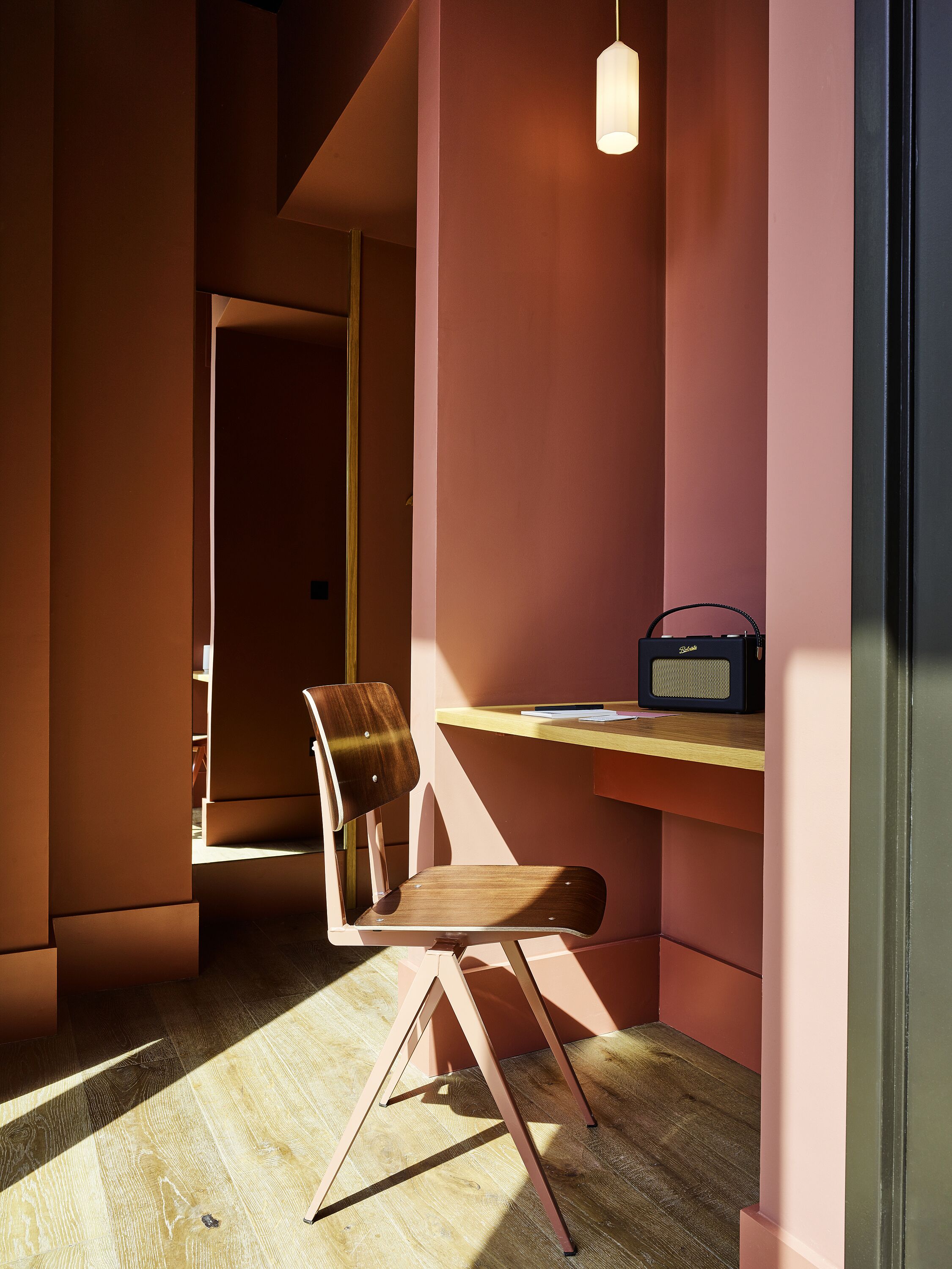 Una habitación con una silla de madera, un escritorio con una radio y una lámpara colgante.