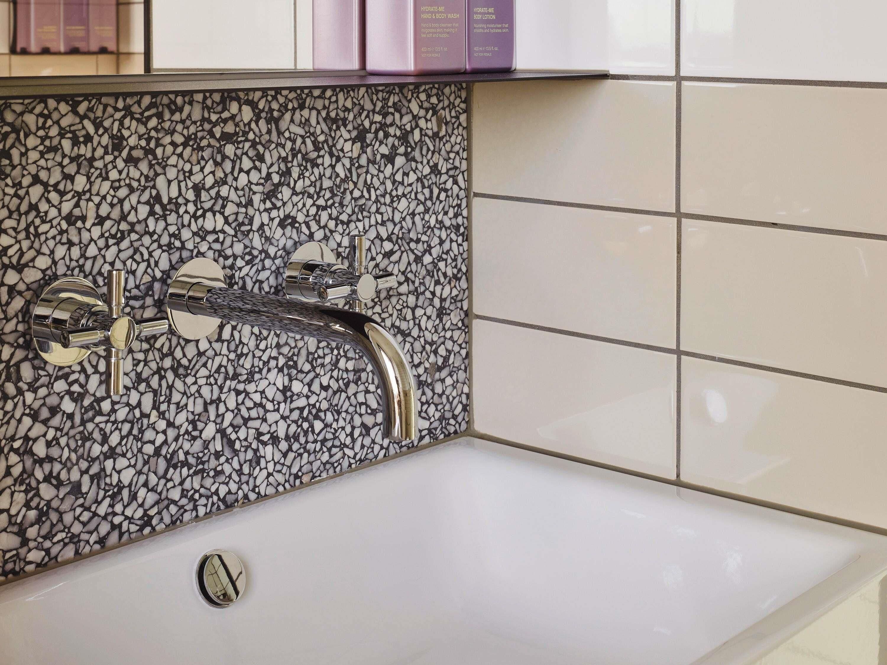 A bathroom with a white sink, a chrome faucet, and a mosaic tile backsplash.