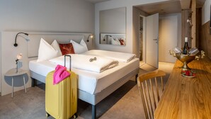Una habitación de hotel con una cama, una mesa de madera, una maleta y un espejo.