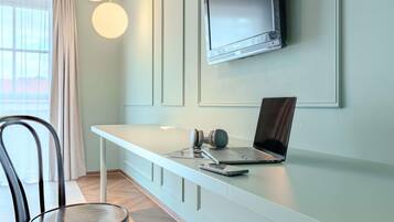 A modern office space with a white desk, a laptop, and headphones. A TV is mounted on the wall above the desk.