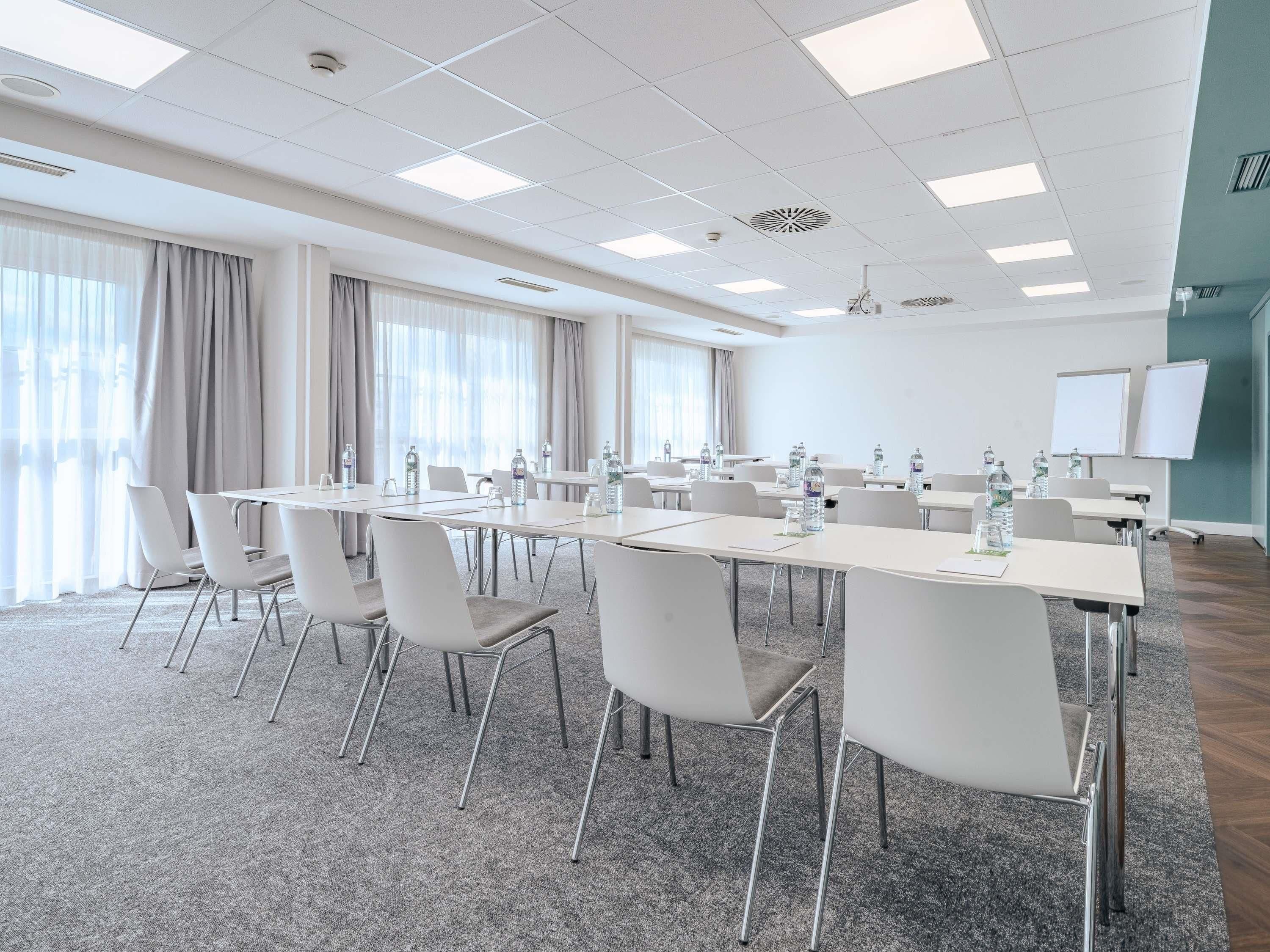 Ein Konferenzraum mit Tischen, Stühlen, Wasserflaschen, einer Tafel und einem Projektor.