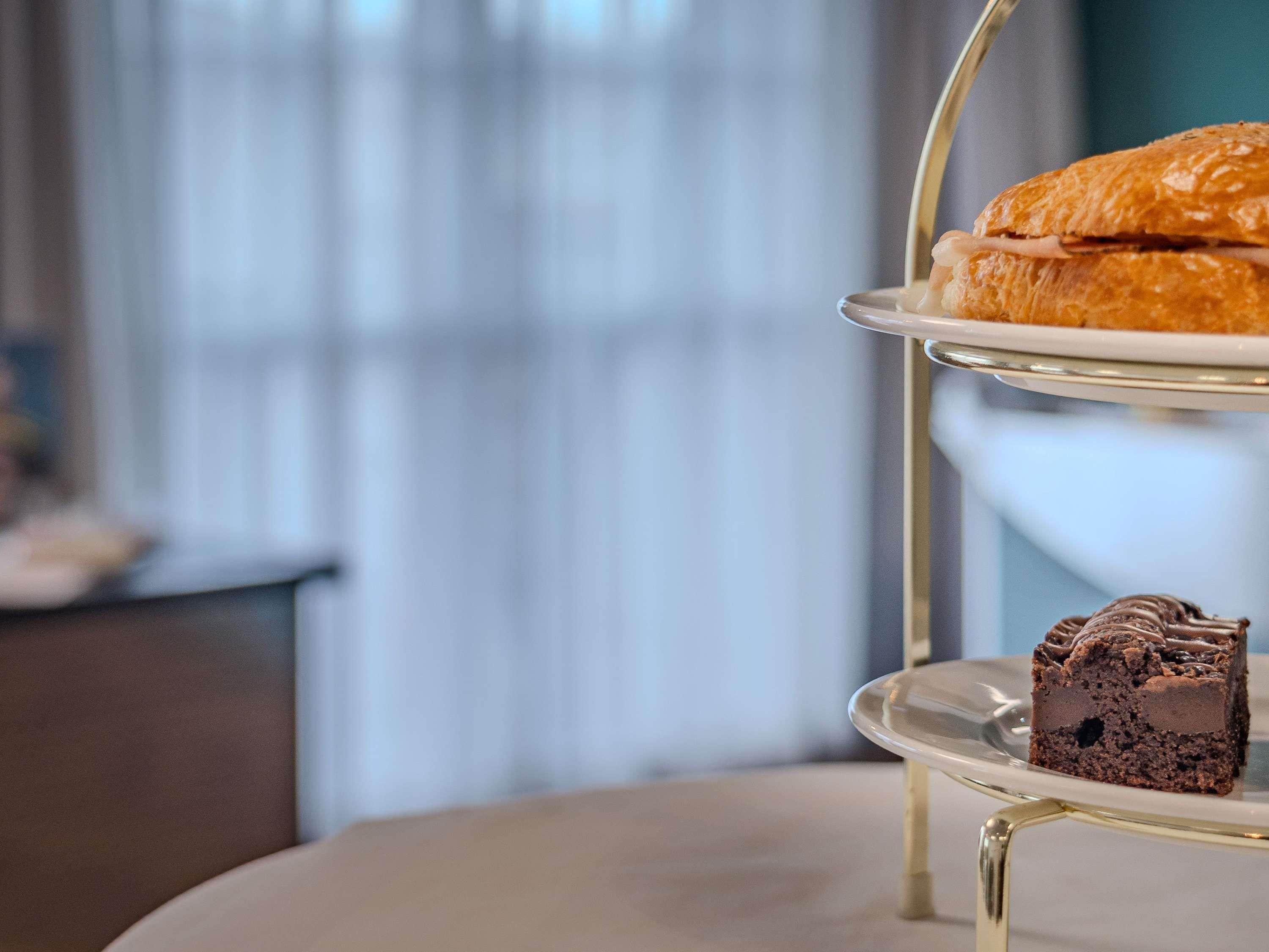 A three-tiered dessert stand with a sandwich and a slice of chocolate cake.