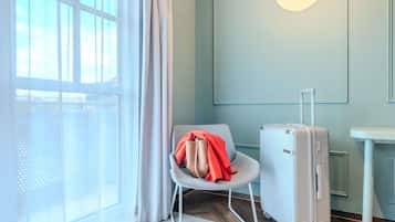 Una habitación con ventana, una silla, una maleta y una mesita.
