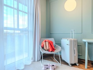 A room with a window, a chair, a suitcase, and a small table.