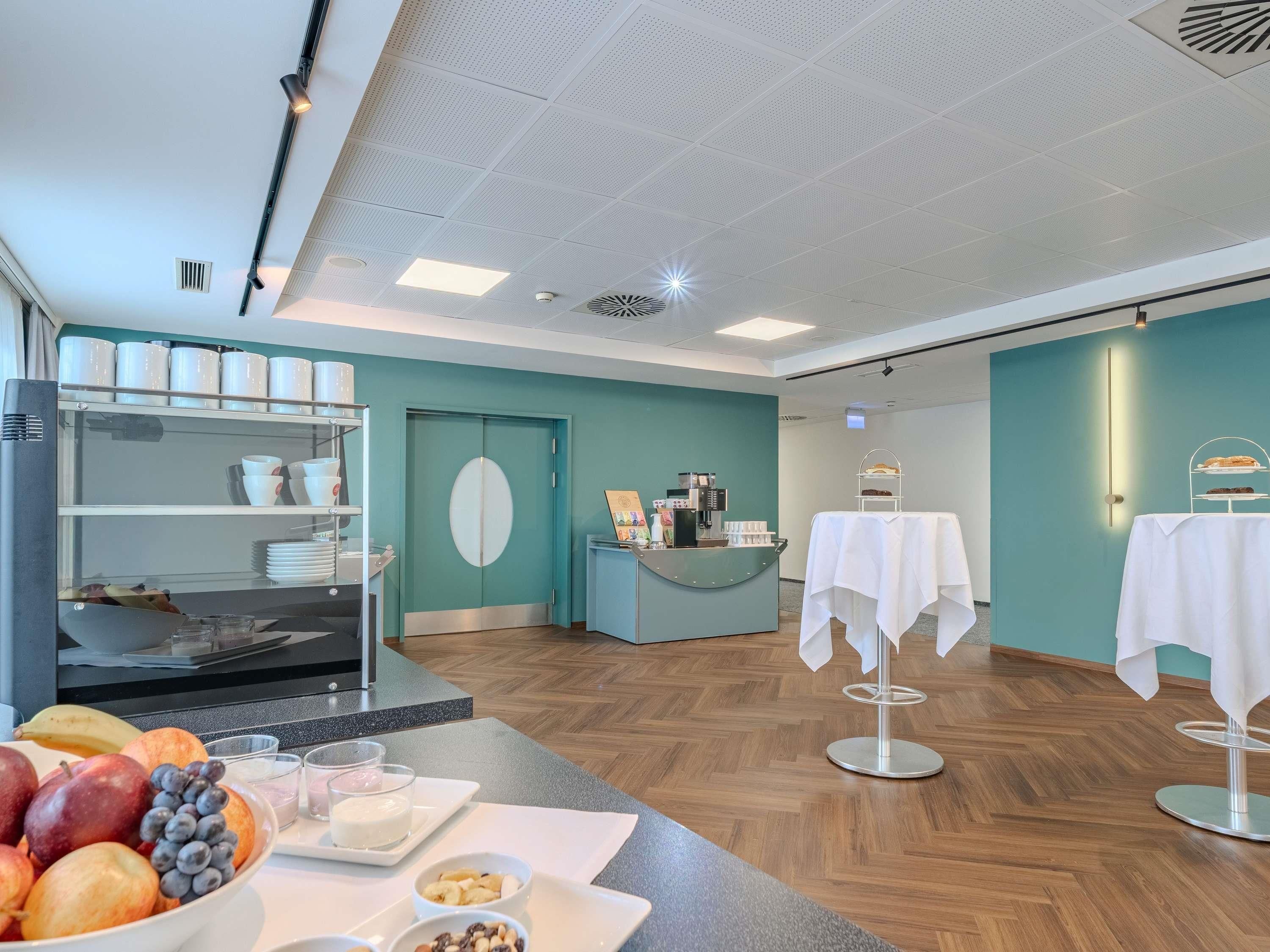 A modern interior with a teal wall, a reception desk, a coffee machine, and a fruit display.
