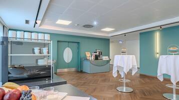 A modern interior with a teal wall, a reception desk, a coffee machine, and a fruit display.