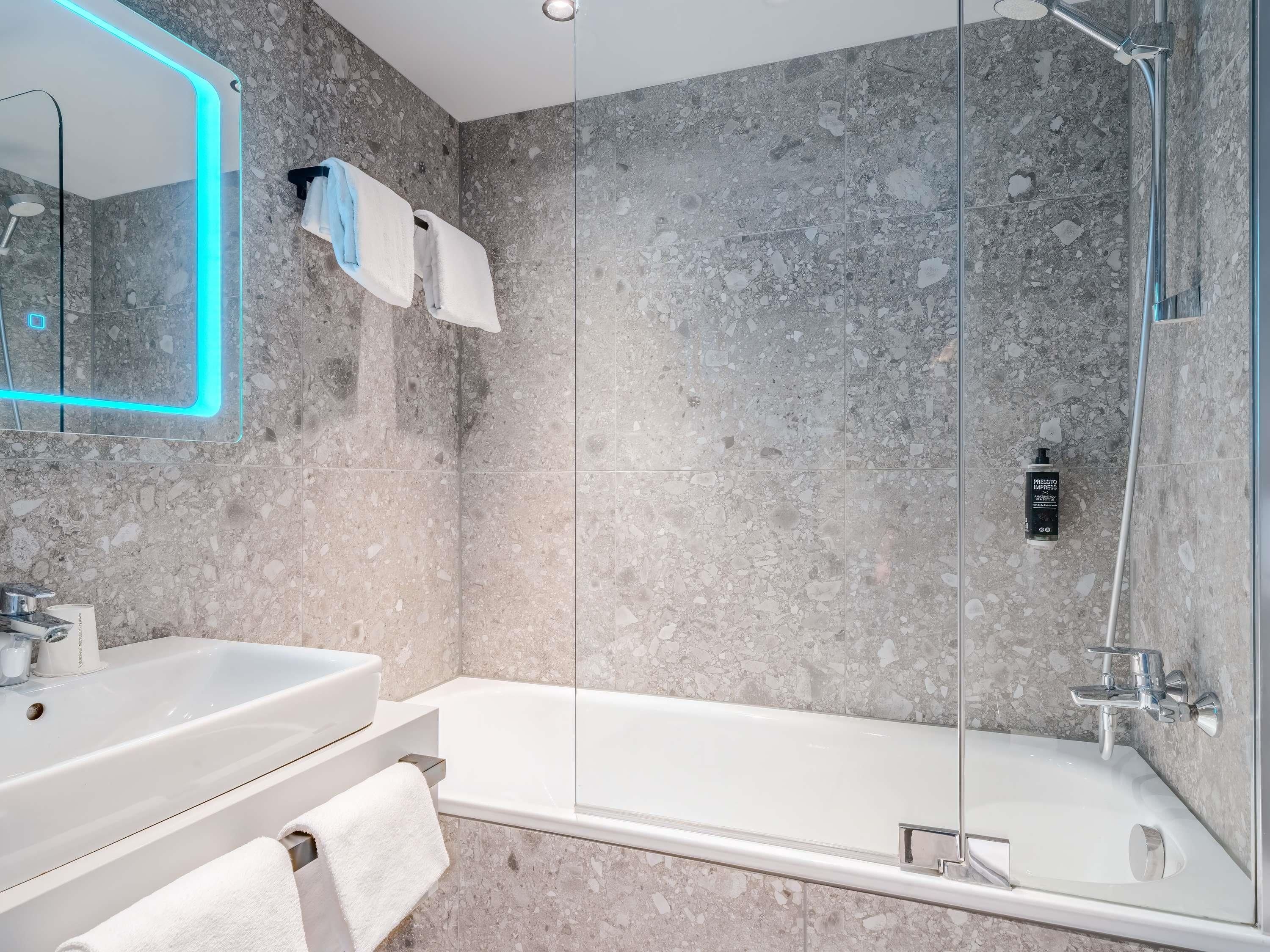 Ein modernes Badezimmer mit einer Duschkabine, einer weißen Badewanne, einem Waschbecken inklusive Spiegel und einem Handtuchhalter.