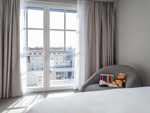 A hotel room with a large window, a grey armchair, and a teddy bear. - Ibis Styles Graz Messe (Graz)