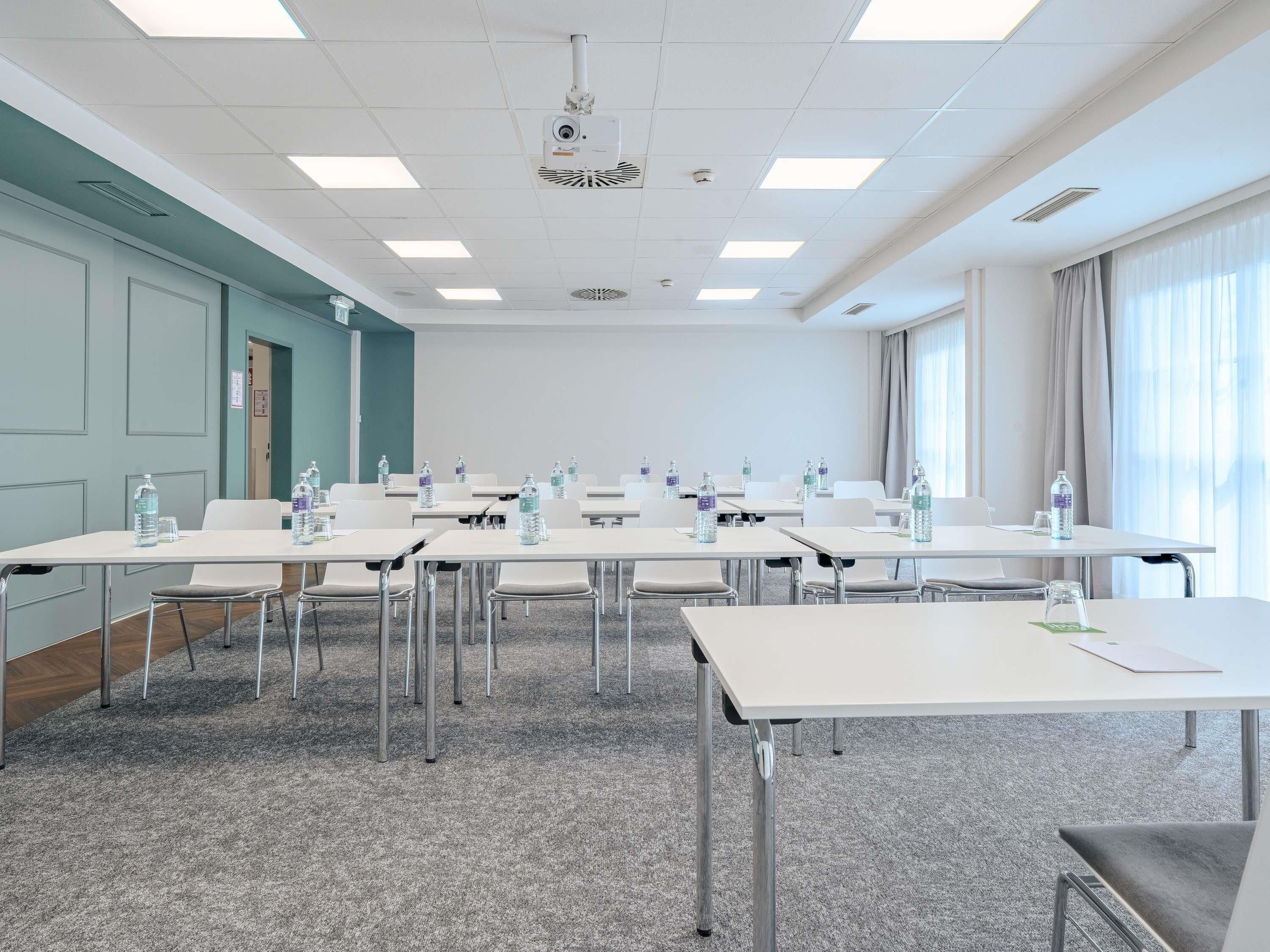 A conference room with white tables, chairs, and a projector on the ceiling.
