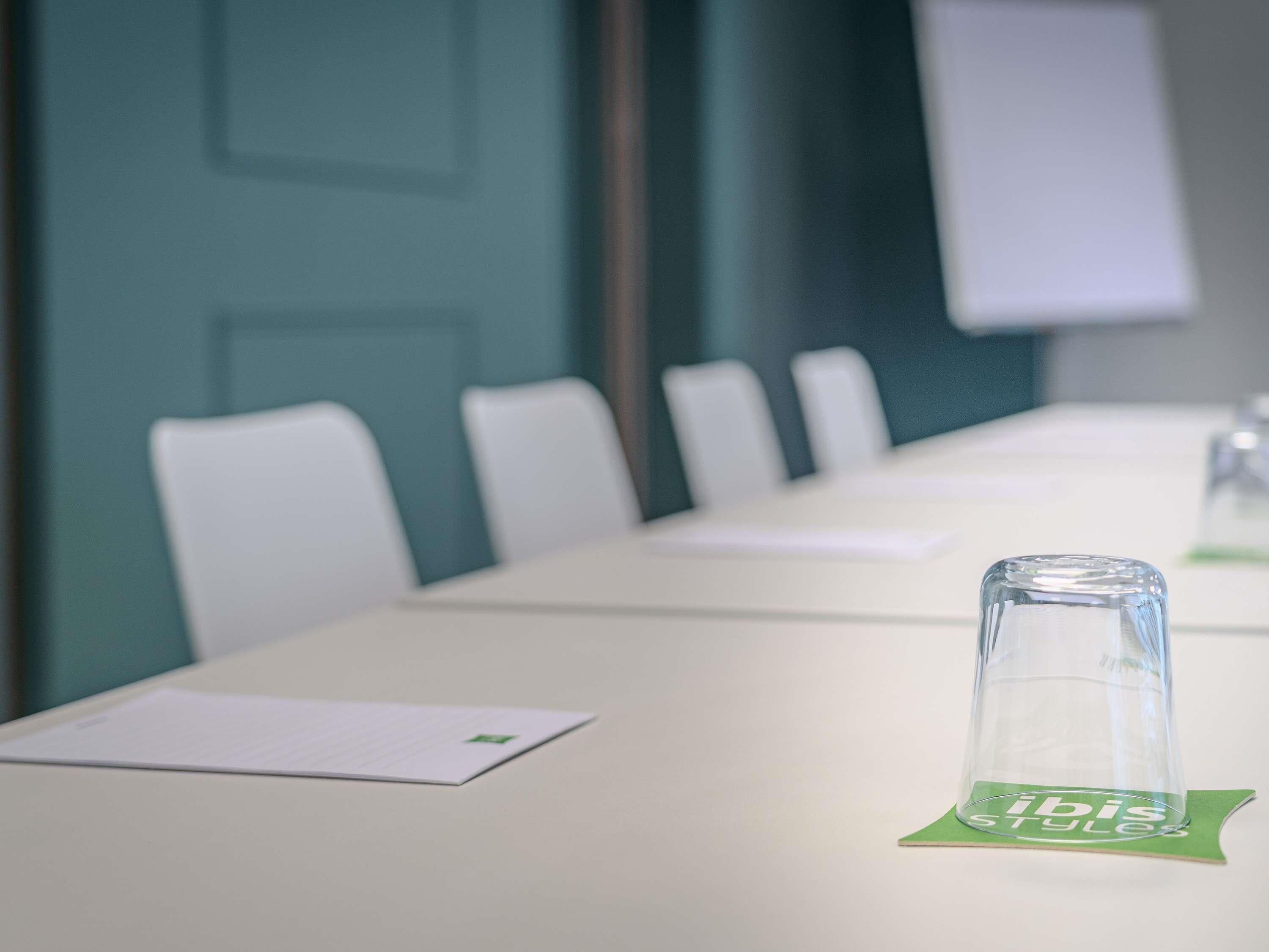 Una sala de conferències amb una taula llarga, cadires i un got sobre un posavasos.