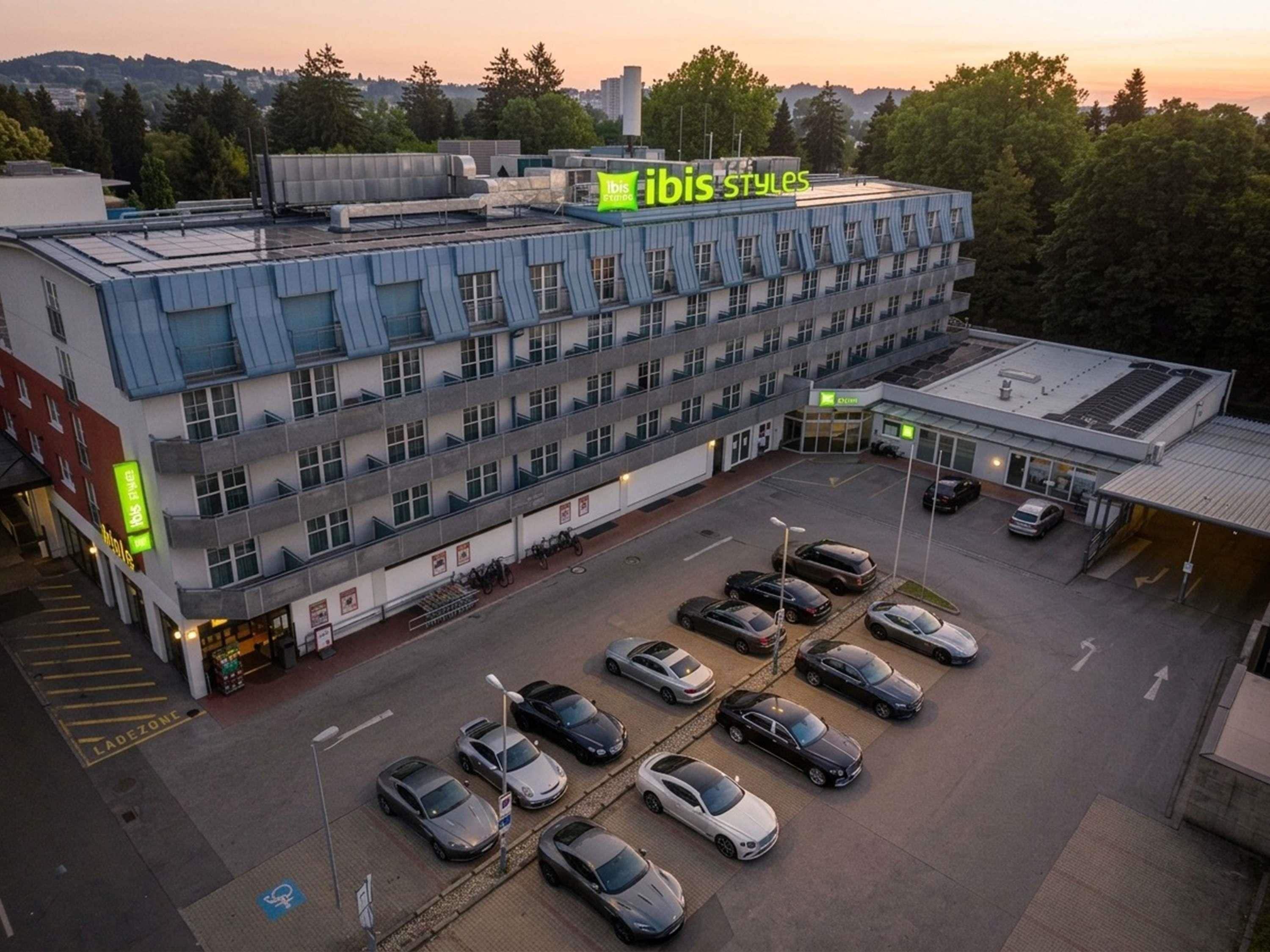Un edificio de varios pisos con estacionamiento, un letrero que dice 'ibis styles' y una entrada visible.